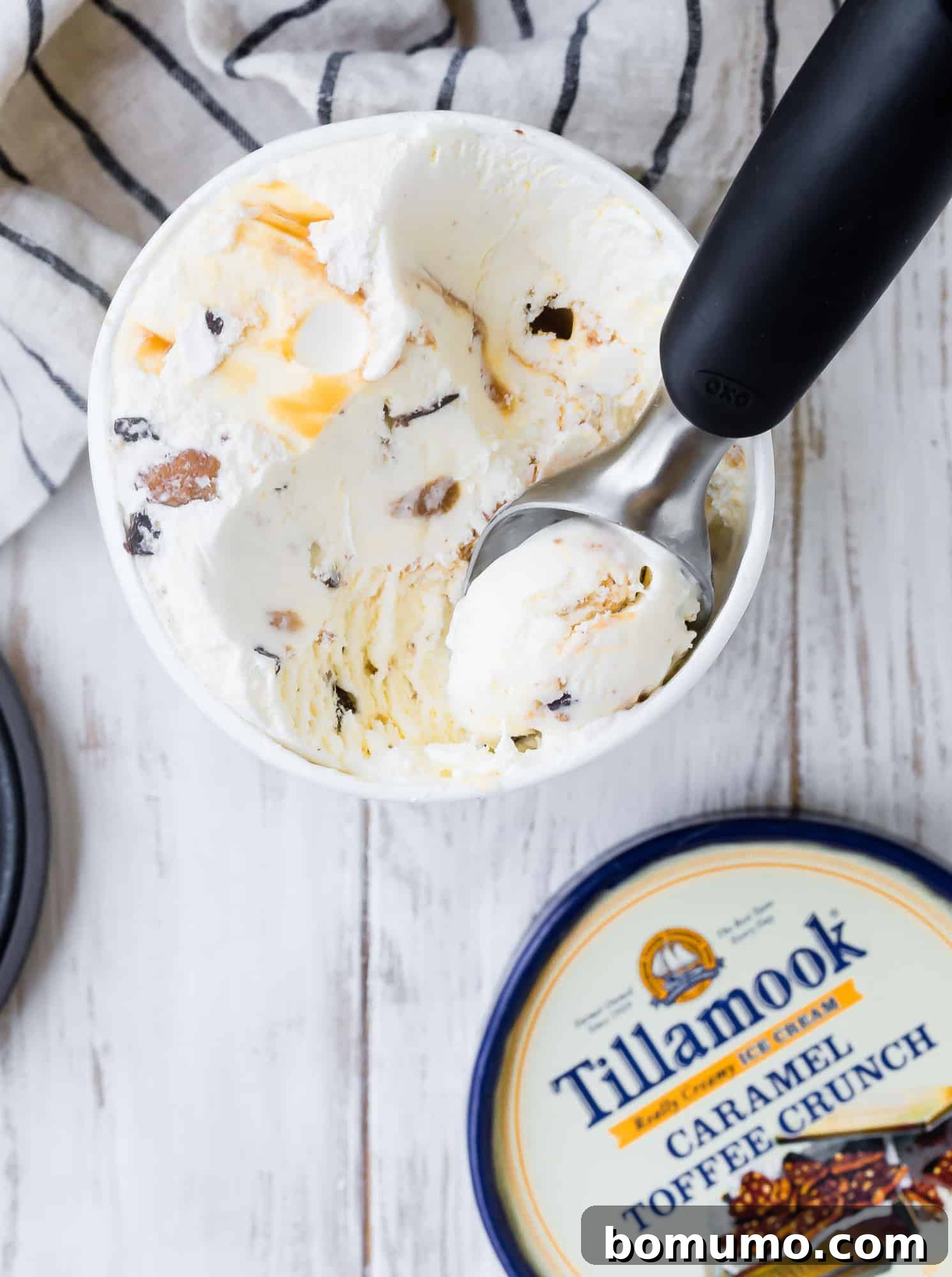 A close-up shot of a hand expertly scooping creamy ice cream from a round cylinder carton, preparing to adorn the freshly grilled pineapple.