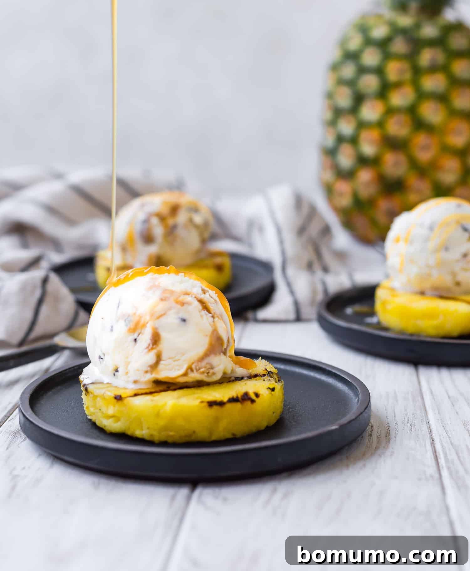 A decadent close-up shot capturing rich, golden caramel being artfully drizzled over a generous scoop of ice cream nestled atop a warm, grilled pineapple slice.