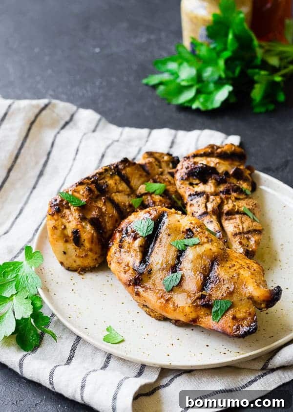 Three portions of honey mustard chicken on a white plate, elegantly garnished with fresh parsley, ready to serve.