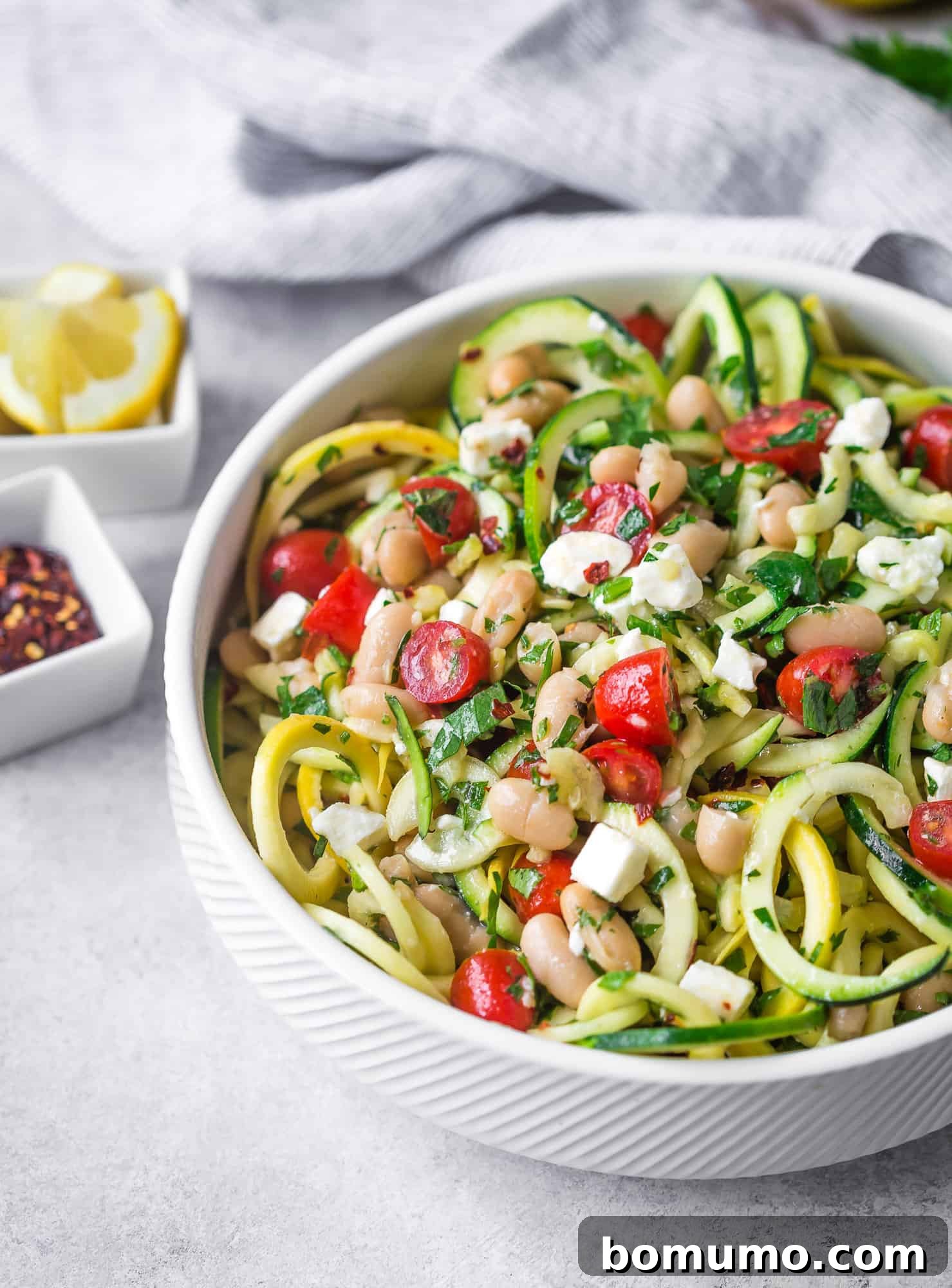 Zucchini noodle salad with fresh herbs, tomatoes, white beans, garnished with feta.