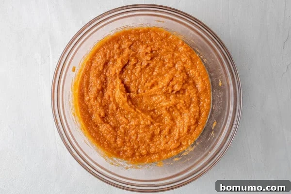 Wet ingredients mixed smoothly together in a clear glass bowl, showcasing the rich pumpkin color.
