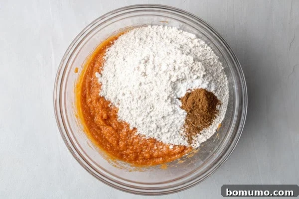 Dry ingredients carefully added on top of the wet ingredients in a glass mixing bowl, poised for gentle mixing.