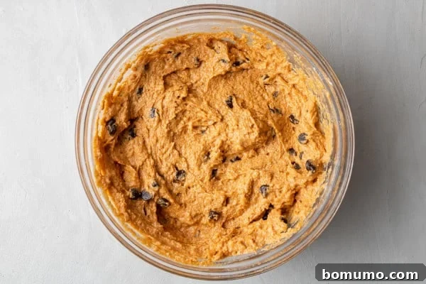 Pumpkin muffin batter in a clear glass mixing bowl, showing the combined wet and dry ingredients.