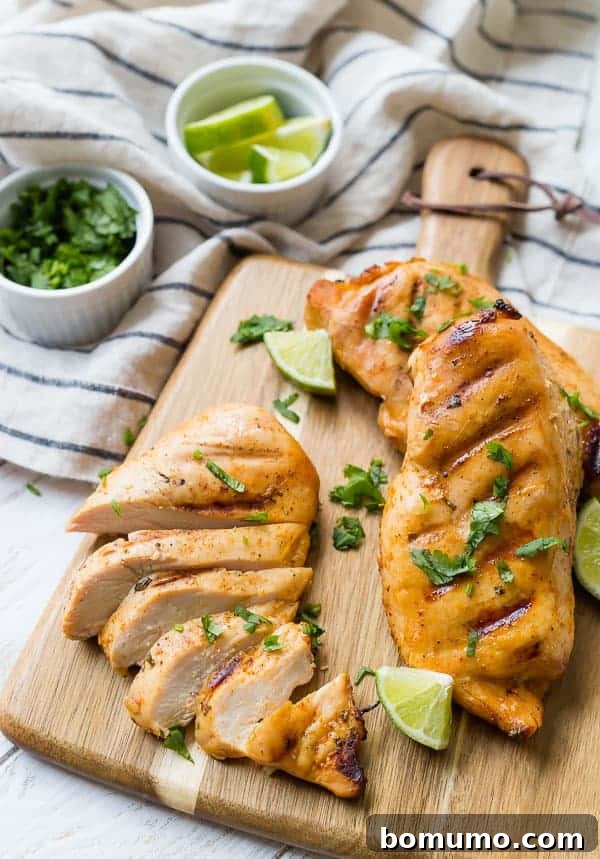 Three chicken breasts, one sliced, on a cutting board with lime and cilantro sprinkled around.