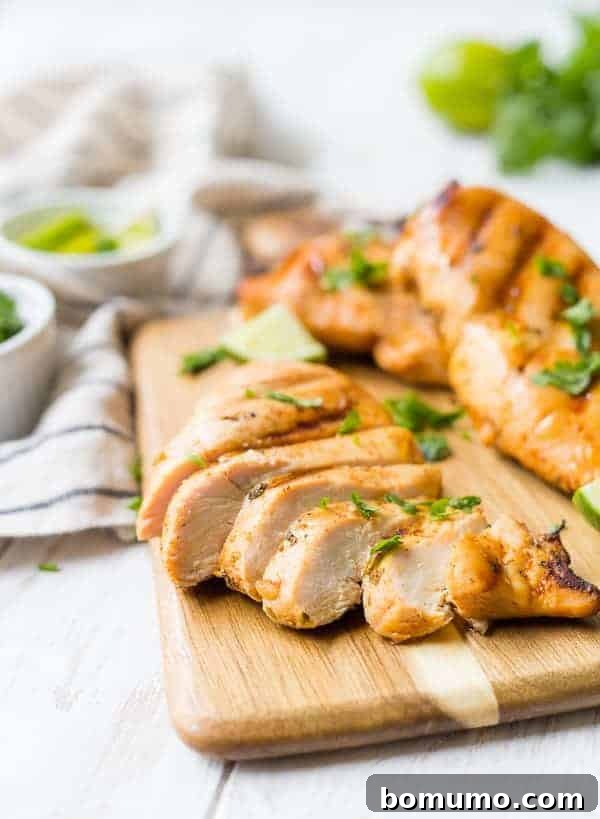 A sliced chicken breast on a cutting board, two other chicken breasts are pictured. They are all sprinkled with fresh cilantro leaves.