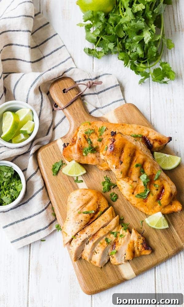 Overhead view of three grilled chicken breasts on a wooden cutting board with a handle. One chicken breast is sliced. All are sprinkled with fresh cilantro.