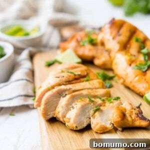 Grilled chicken breasts on a wooden cutting board. Chicken breast in the foreground is sliced.