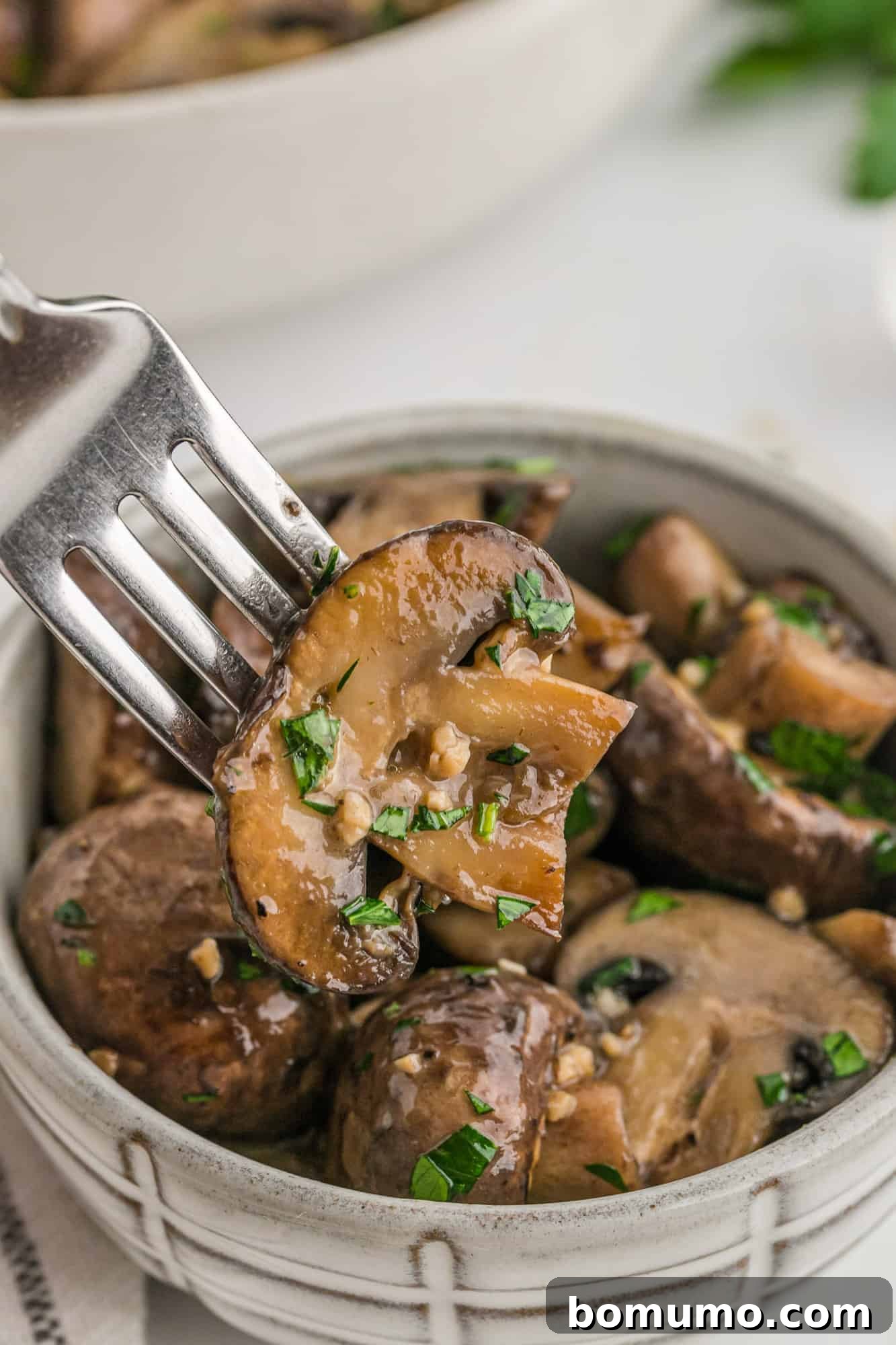 Sautéed mushroom on a fork, glistening with garlic butter.