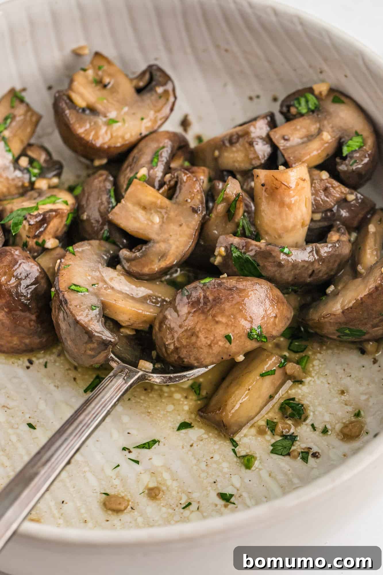 Sautéed mushrooms in a white bowl, garnished with fresh parsley and a rich garlic butter sauce.