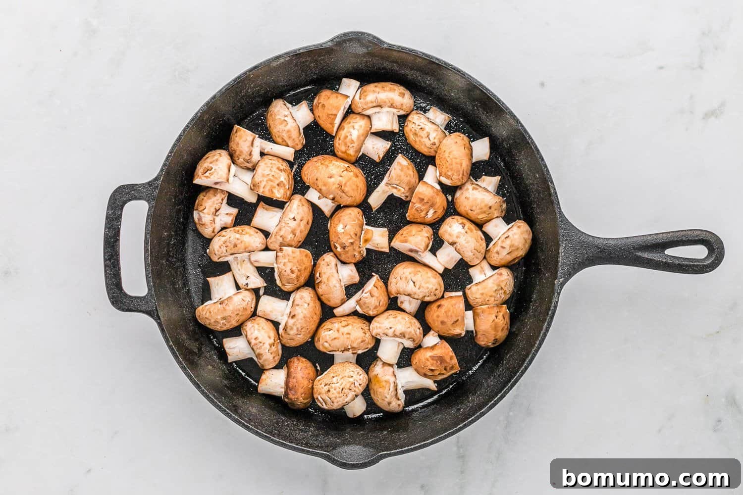 Halved mushrooms evenly spread in a hot skillet, beginning to sear.