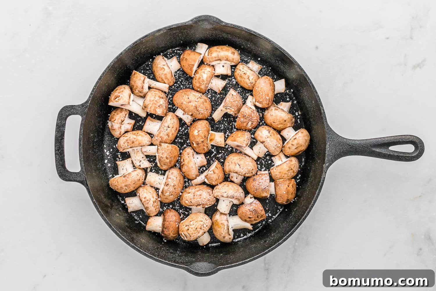 Mushrooms in a skillet, showing early stages of golden-brown caramelization.