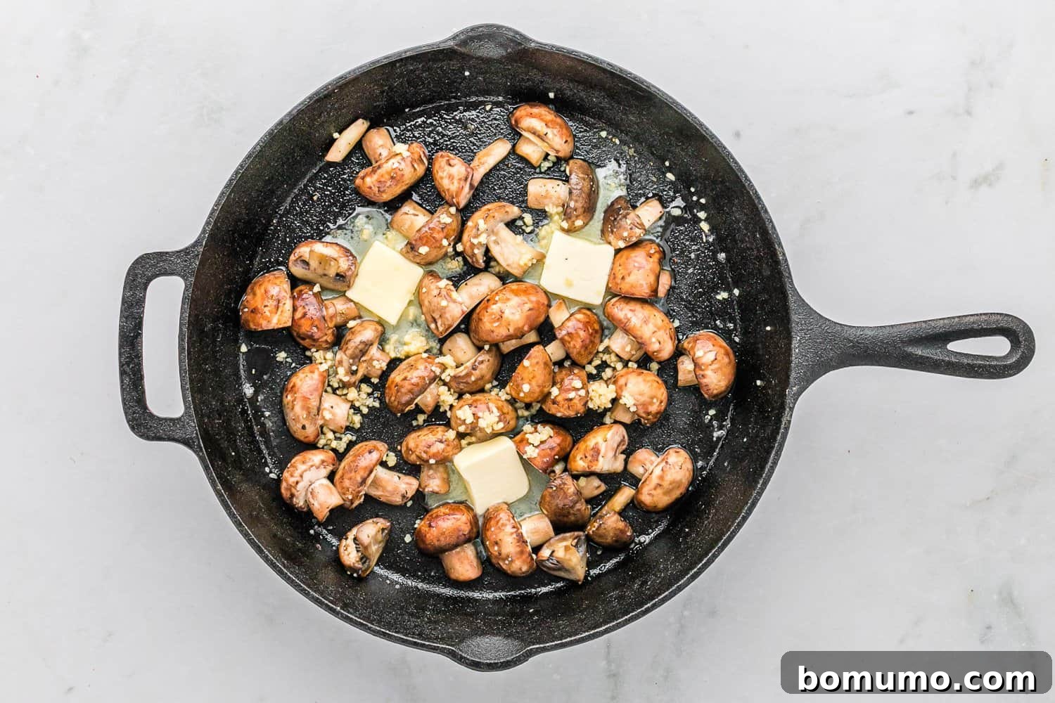 Unmelted butter and garlic added to the sautéed mushrooms in a pan.