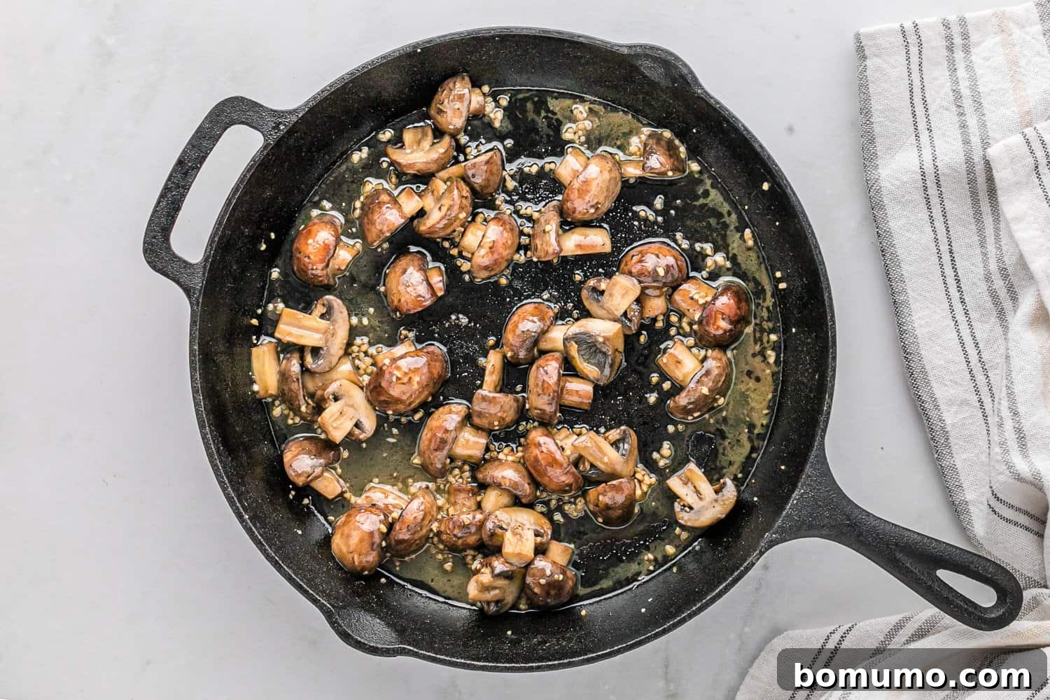 Sautéed mushrooms coated in melted garlic butter sauce in a pan.