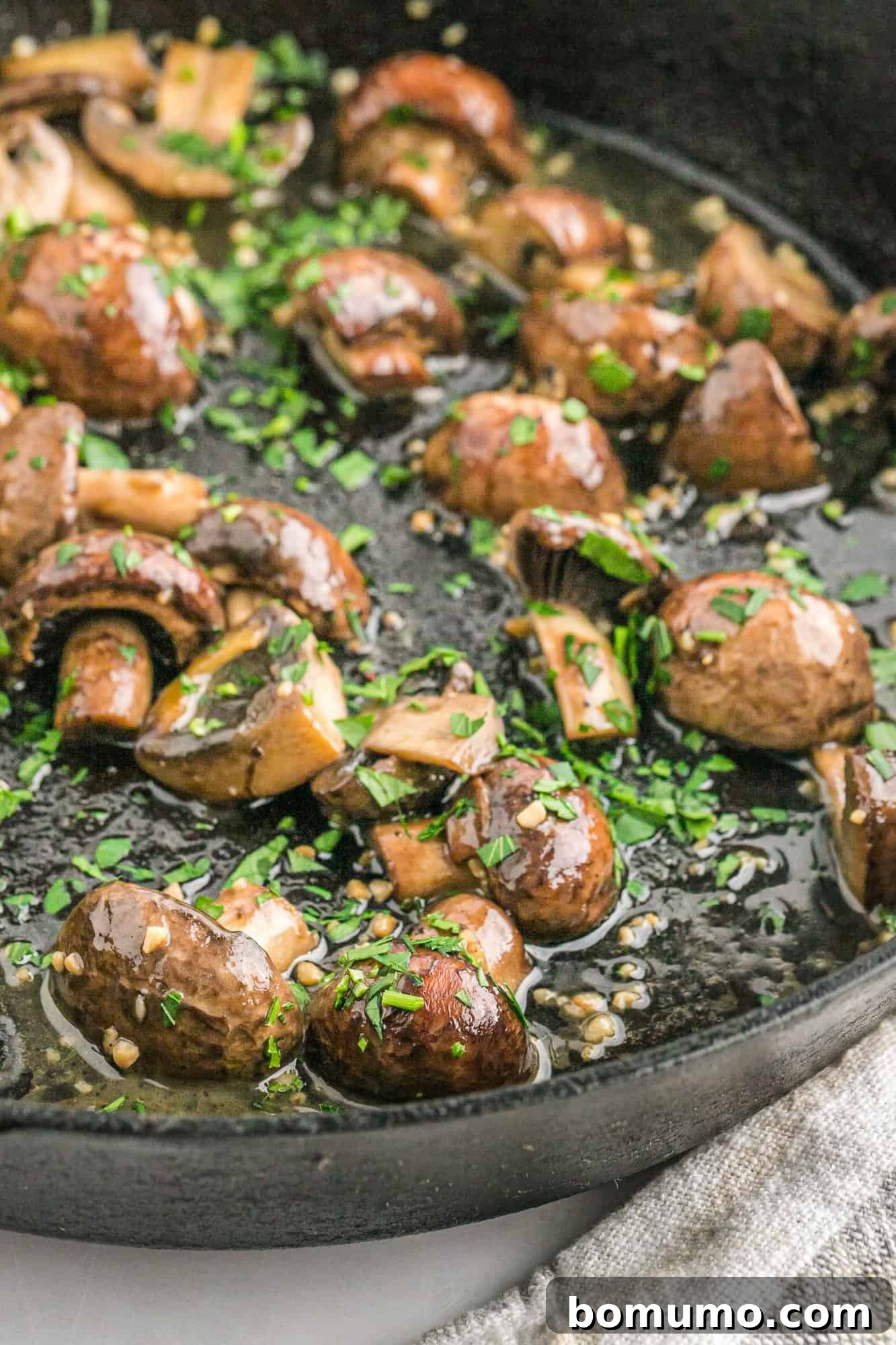 Cooked mushrooms swimming in garlic butter and garnished with fresh parsley.