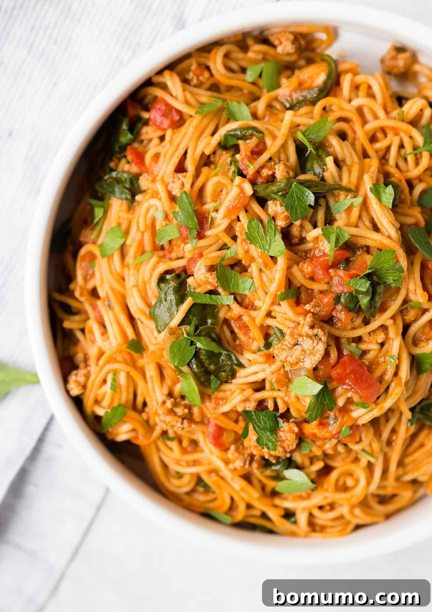 Overhead view of perfectly cooked Instant Pot spaghetti and a rich meat sauce in a white serving bowl, elegantly garnished with fresh parsley and grated Parmesan cheese.