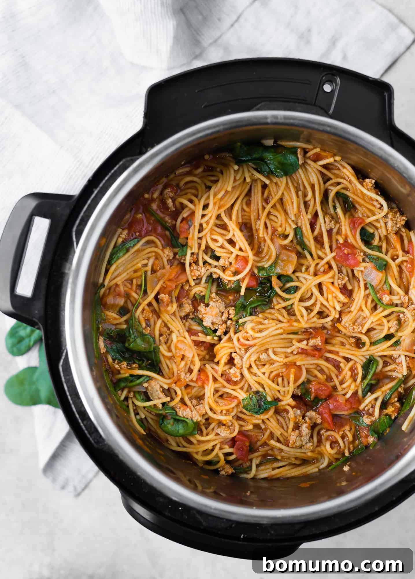 Overhead view of savory spaghetti in an Instant Pot, mixed with a rich meat sauce and vibrant spinach, freshly cooked and ready to serve.