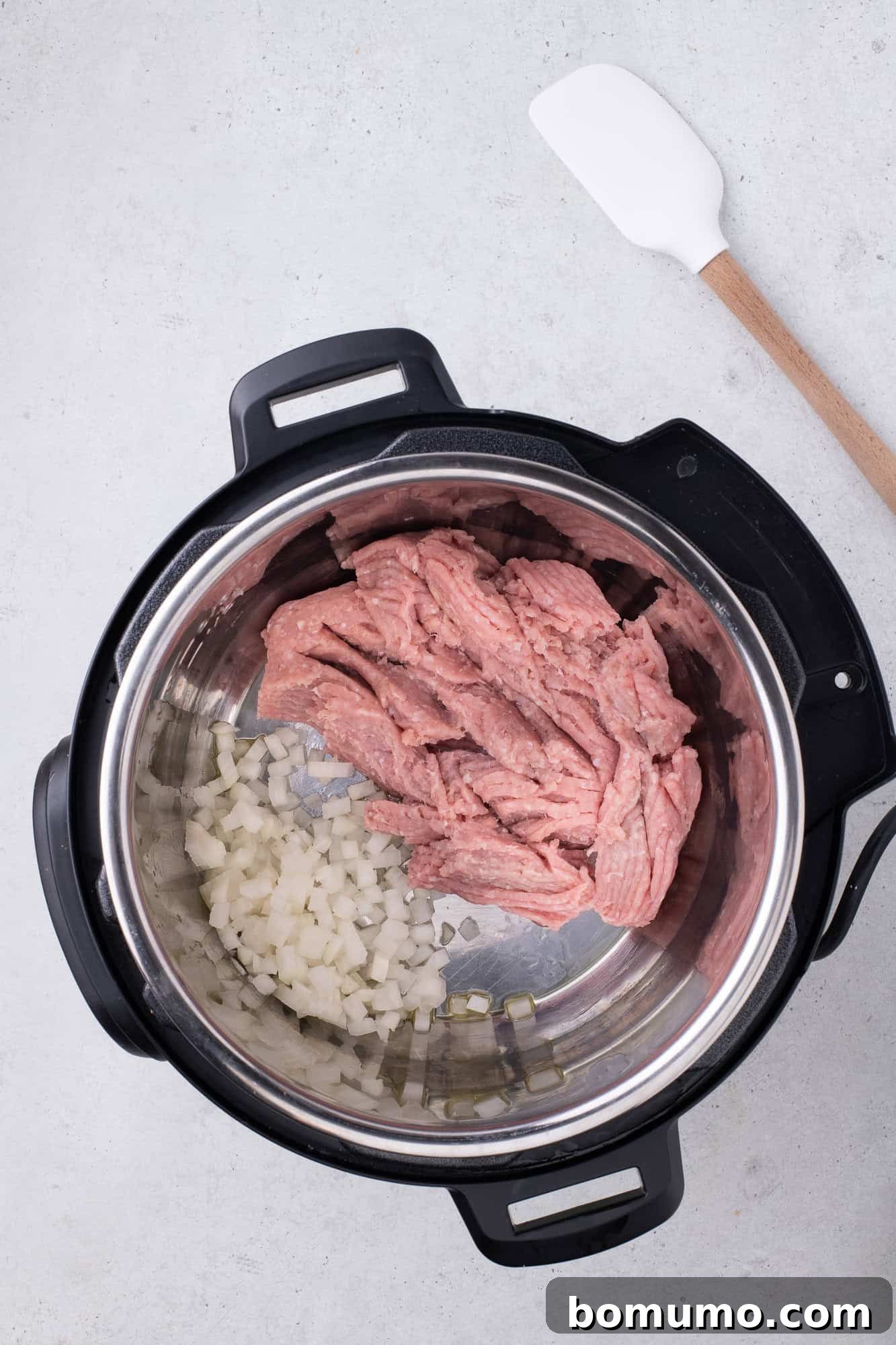 Uncooked ground turkey and chopped onions placed in the Instant Pot, prior to sautéing, ready to form the flavorful base of the spaghetti.