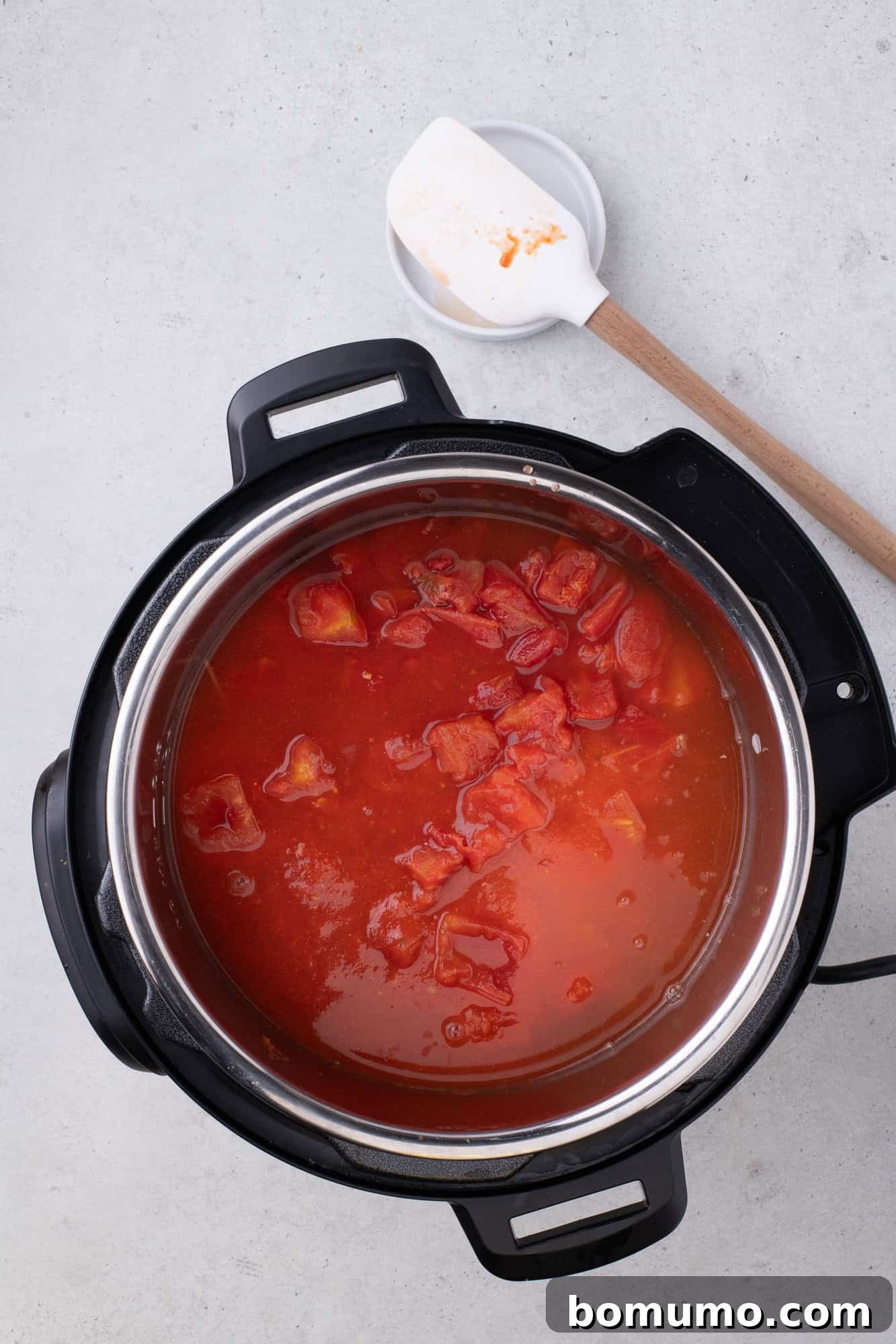 Rich tomato sauce, water, and diced tomatoes poured over spaghetti and meat in the Instant Pot, ensuring all ingredients are fully immersed and ready for pressure cooking.