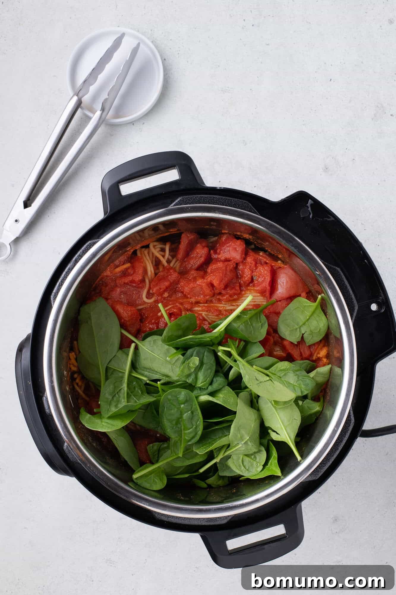 Fresh spinach leaves added to the hot Instant Pot Spaghetti, awaiting wilting, poised to add a healthy and vibrant touch to the meal.