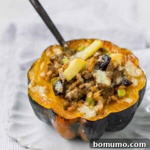 Stuffed acorn squash filled with farro, sausage, apples, and cheese on a white plate, with a fork stuck into the filling.