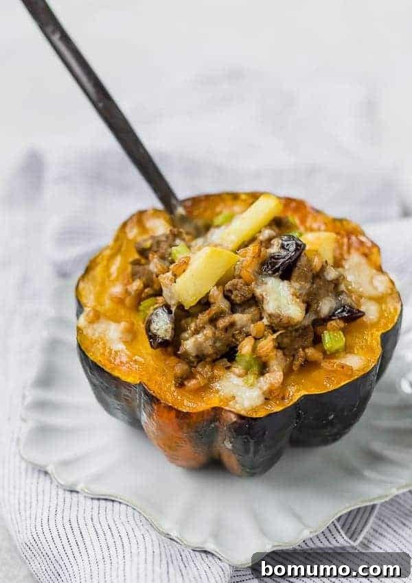 A single stuffed acorn squash half, richly filled with farro, sausage, apples, and melted cheese, sits on a white plate with a fork inserted, ready to be eaten.