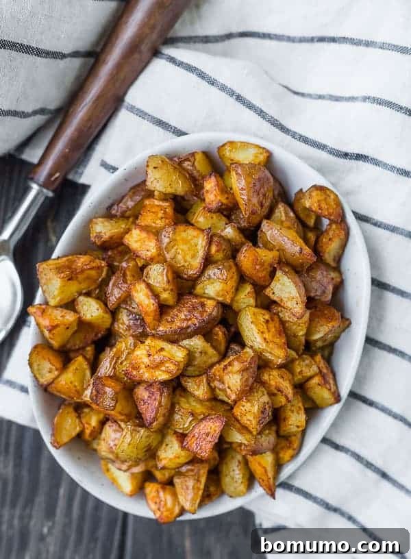 Overhead view of a oval white bowl filled to the brim with golden brown roasted potatoes.
