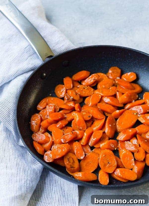 Richly glazed sliced carrots simmering in a black nonstick skillet, glistening with brown sugar and bourbon.