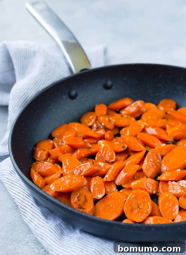 The cooking process of brown sugar bourbon glazed carrots, showing them steaming in a black skillet with the lid slightly ajar.