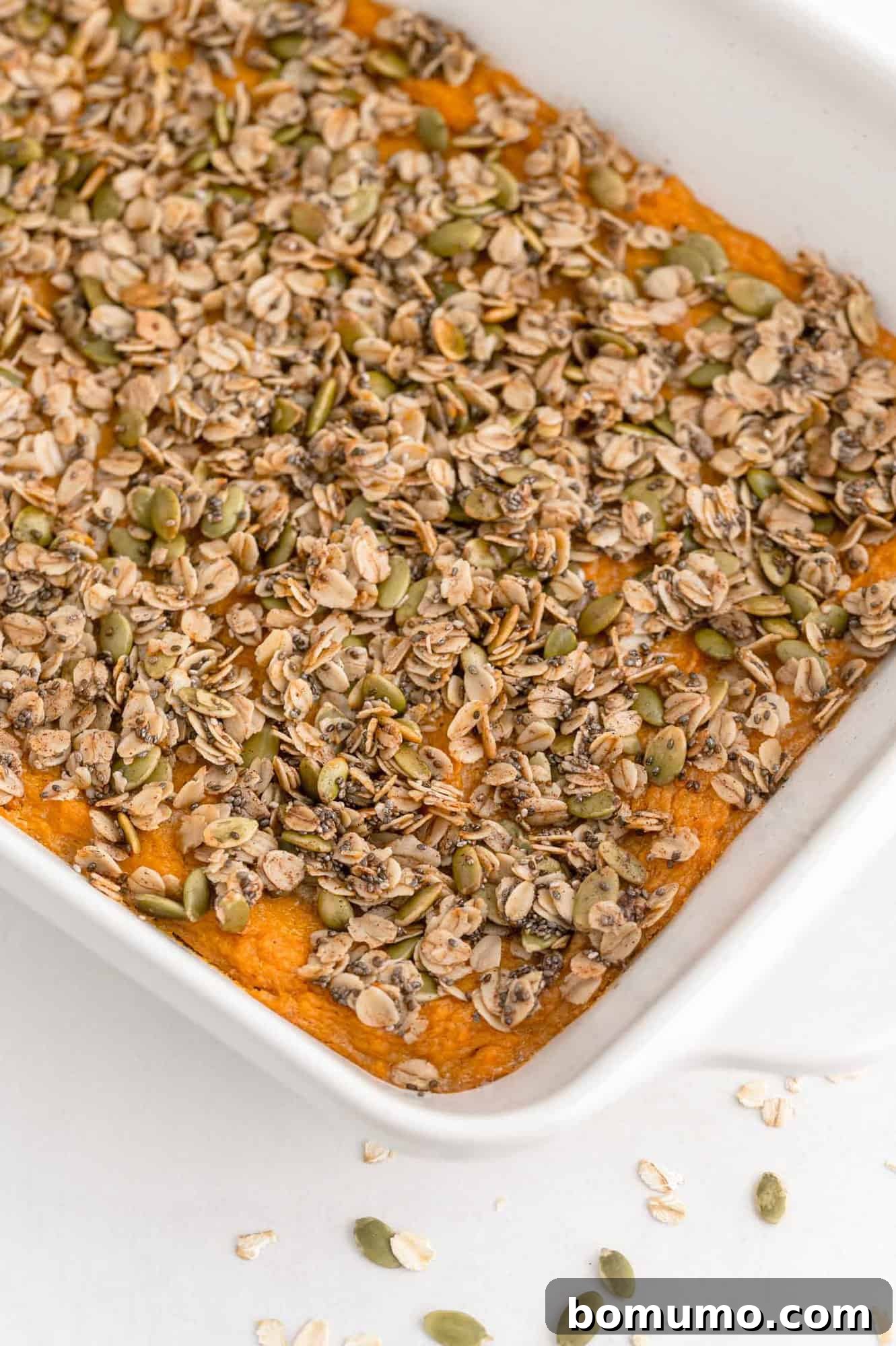 A pristine white casserole dish brimming with healthy sweet potato casserole, crowned with a golden-brown oat topping.