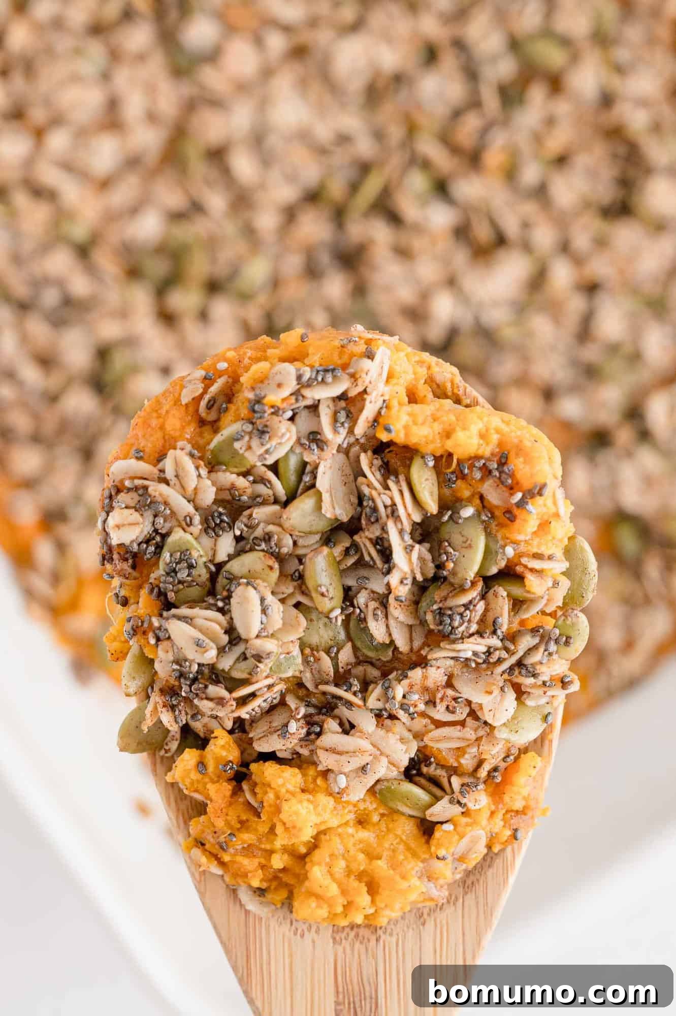 A spoonful of healthy sweet potato casserole, elegantly showcasing its crunchy oat topping, held above the rest of the casserole in a baking dish.