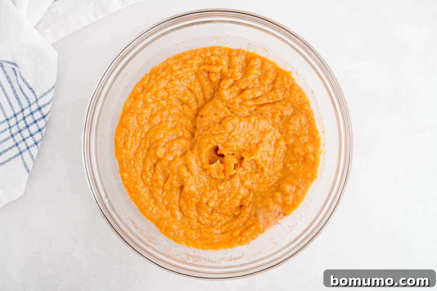 Perfectly mashed sweet potatoes, skillfully blended with eggs and savory seasonings, resting in a clear glass bowl, ready for the next step.