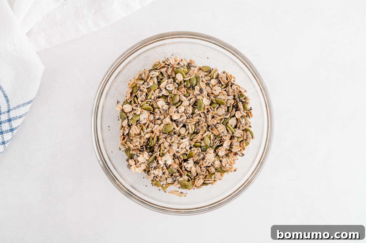 A small, clear glass bowl holding the combined topping ingredients, including hearty oats and vibrant pumpkin seeds, perfectly mixed and ready.
