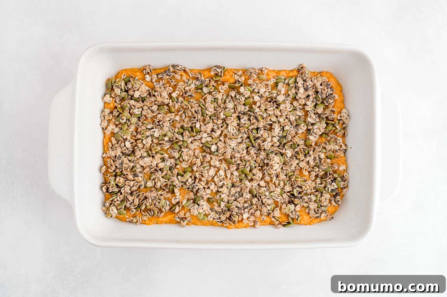 The unbaked healthy sweet potato casserole, featuring its creamy base and vibrant oat topping, nestled in a pristine white baking dish.