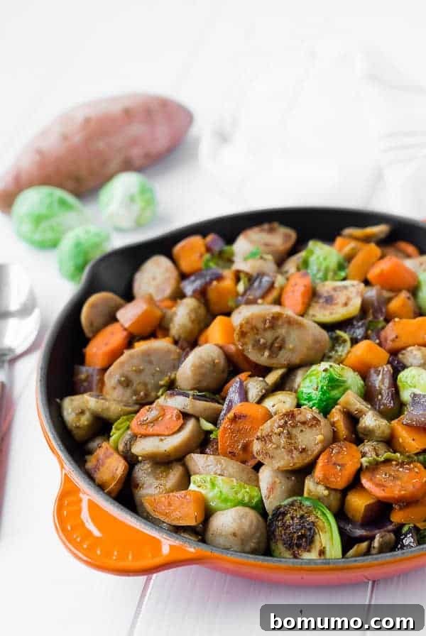 Image of a vibrant one-pan sausage and fall vegetable dinner, featuring caramelized Brussels sprouts, sweet potatoes, and mushrooms, served in an orange cast iron skillet.