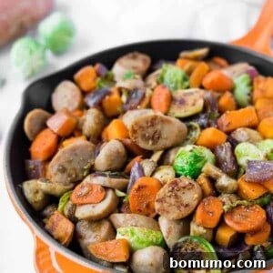 Sausage and fall vegetables glistening in an orange cast iron skillet, ready to be served.