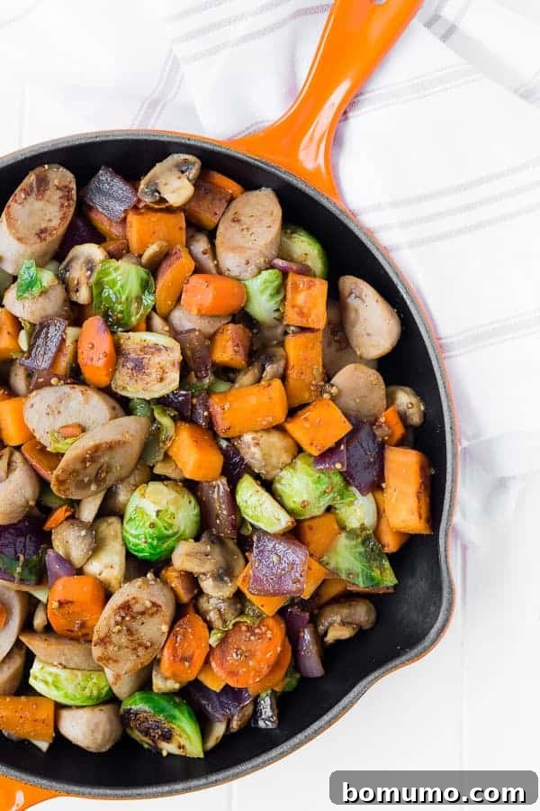 Overhead shot of the completed one-pan sausage dinner, showcasing the harmonious blend of browned sausage and tender, caramelized fall vegetables in a rustic orange cast iron skillet.