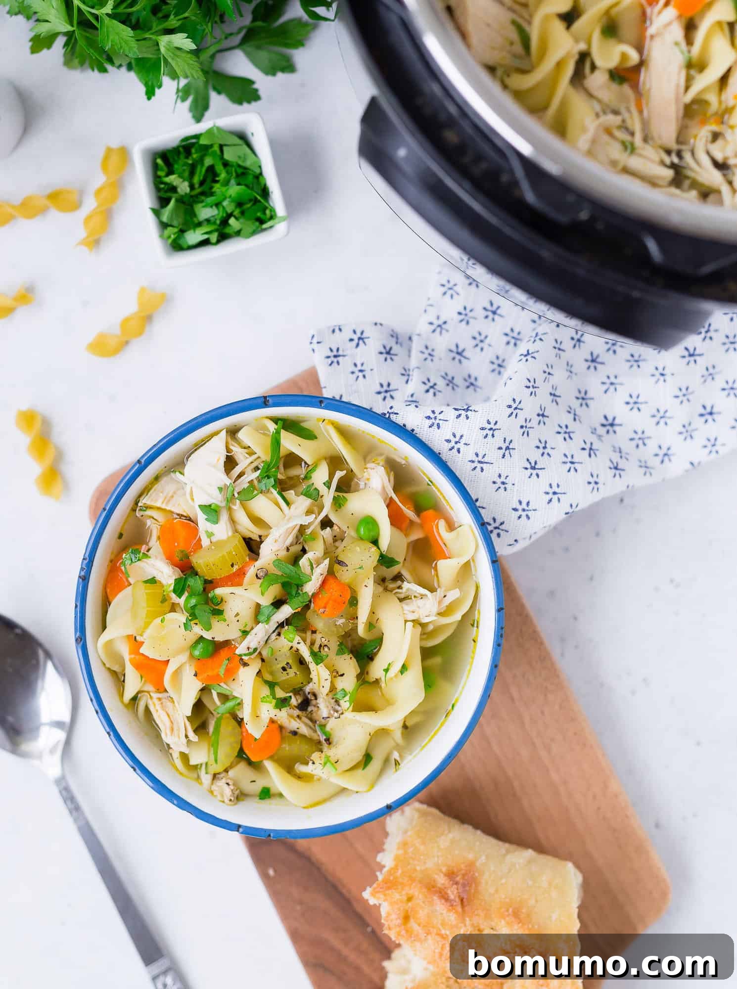 An overhead view of a rustic table setting featuring a bowl of chicken noodle soup, crusty bread, and an Instant Pot.