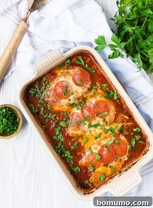 Overhead view of a rectangular baking dish filled with baked pizza chicken, garnished with fresh green parsley.