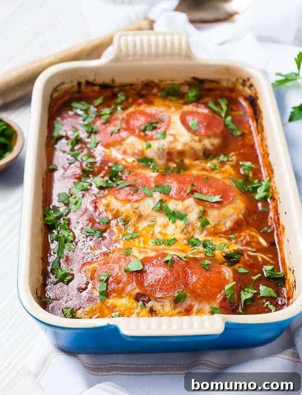 Front view of a blue baking dish showcasing perfectly baked chicken breasts, ready to be topped with cheese and pepperoni.
