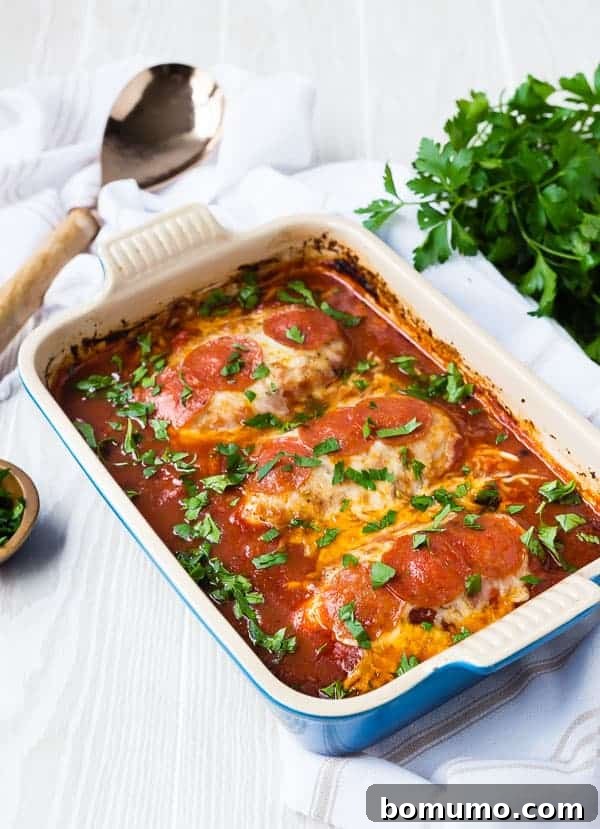 Three perfectly seasoned boneless, skinless chicken breasts nestled in a rich tomato sauce in a blue rectangular baking dish, prior to baking.