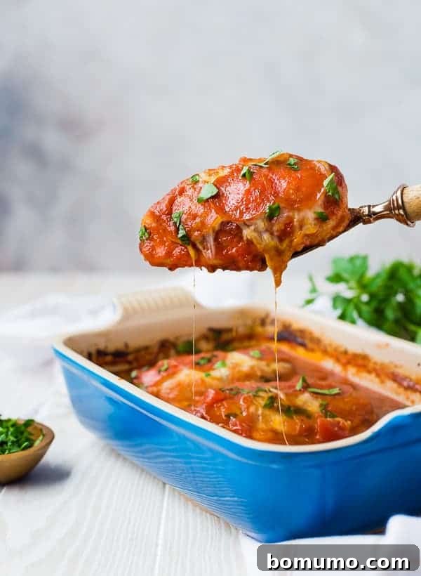 Front view of a portion of baked pizza chicken being scooped out of a baking dish, highlighting the melted cheese and juicy chicken.