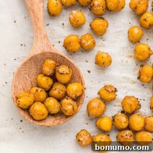 Roasted chickpeas on a wooden spoon, more on parchment lined baking sheet, ready for serving.