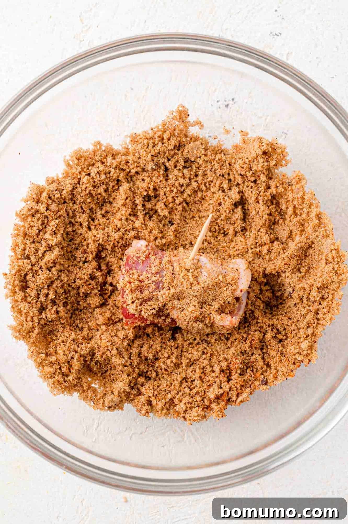 Bacon wrapped date being rolled in sugar spice mixture.