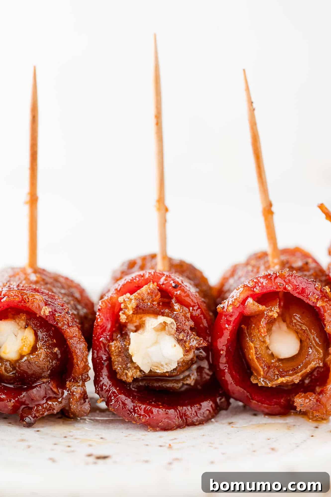 Three bacon wrapped dates on a plate, turned to show filling. 
