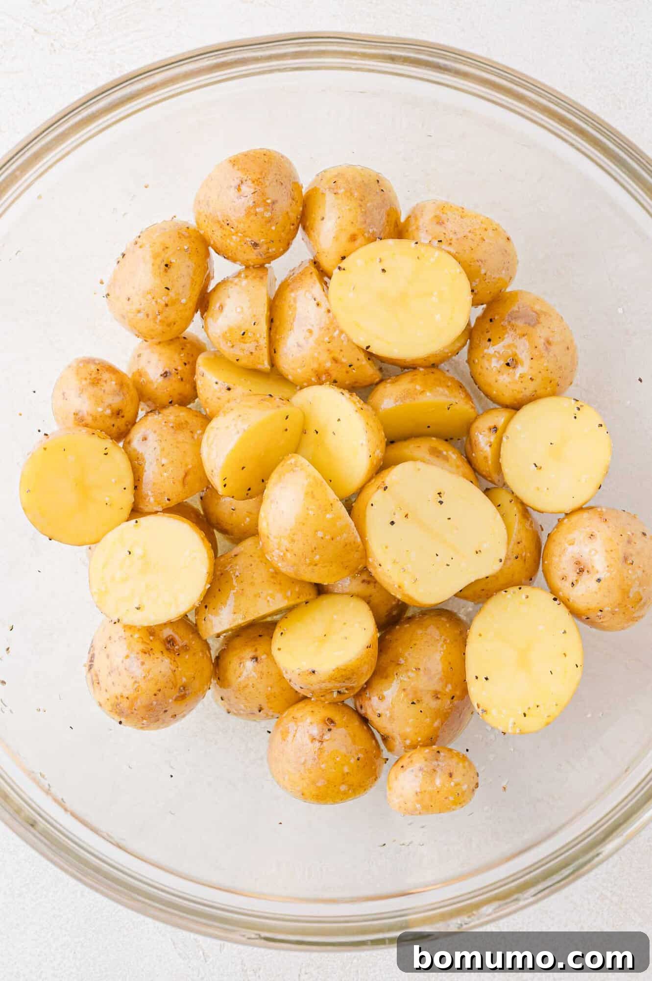 Bowl of halved baby potatoes seasoned with salt and pepper.