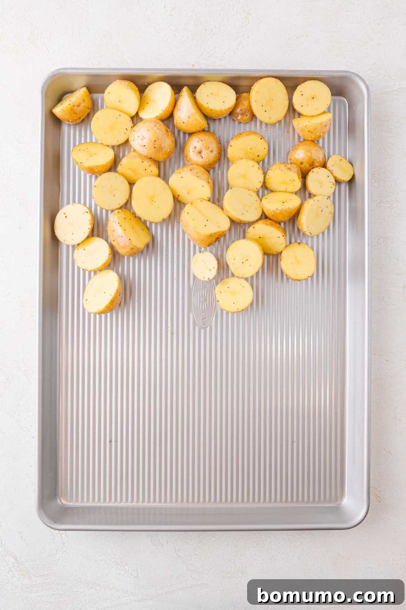 Halved small potatoes scattered on a ribbed baking sheet, ready for roasting.