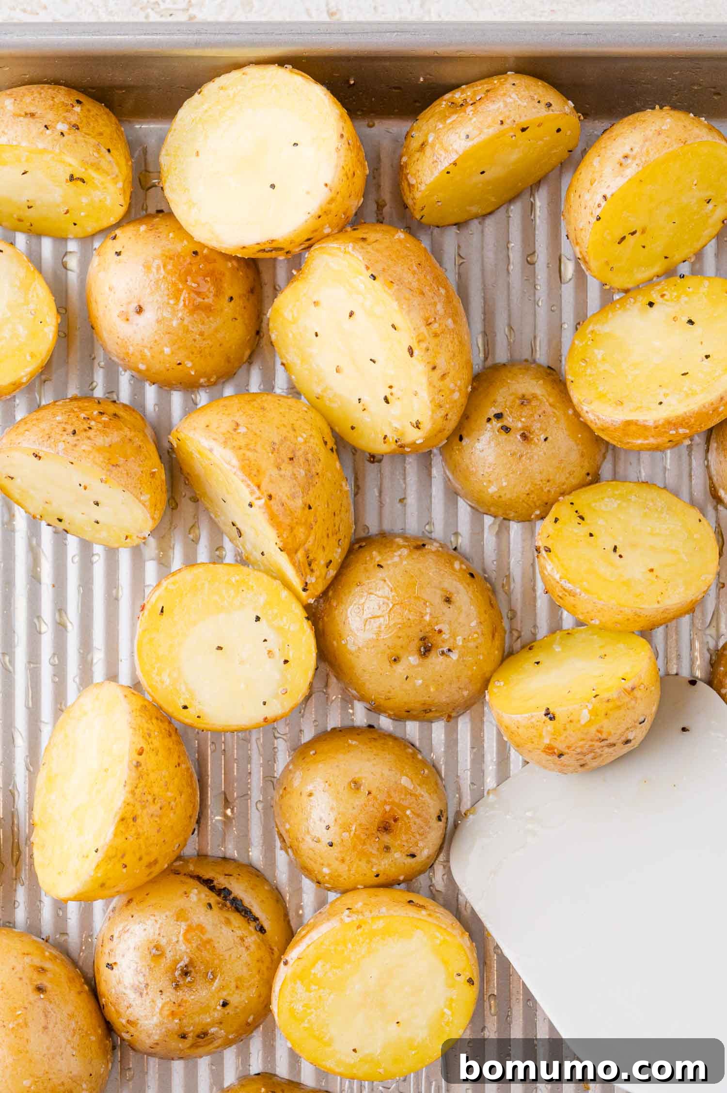 Halved roasted potatoes with salt and pepper on a baking sheet.
