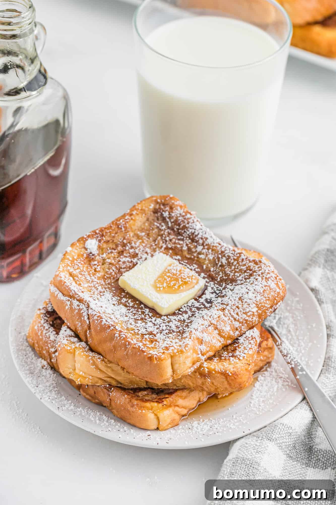 French toast stacked on a plate with powdered sugar, butter, and maple syrup.