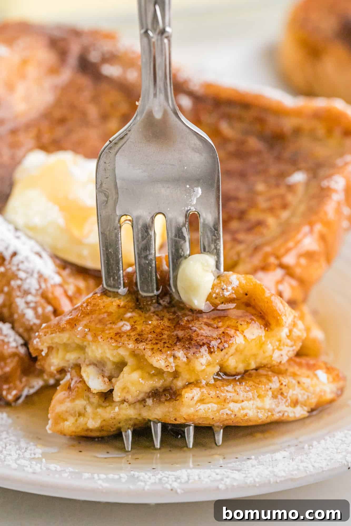 A fork stuck into a slice of French toast to show the texture.