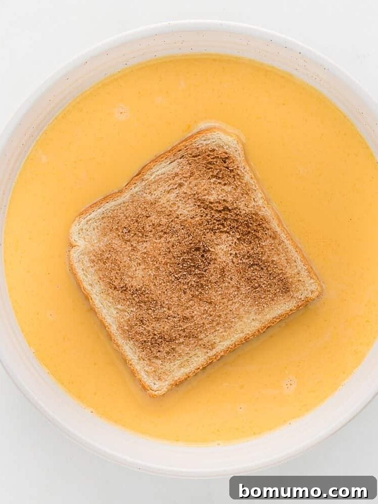 A bread slice dipped in a bowl of egg mixture.